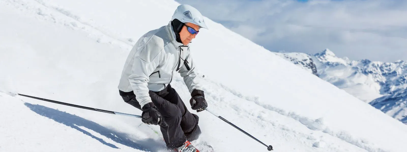 lyžař v bílé bunde sjíždí kopec